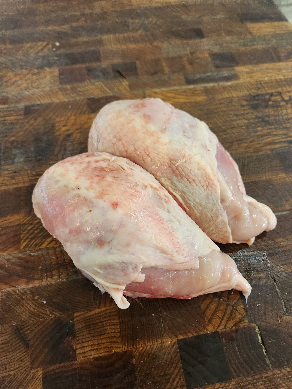 Two raw bone-in chicken breast crowns on a wooden butcher block