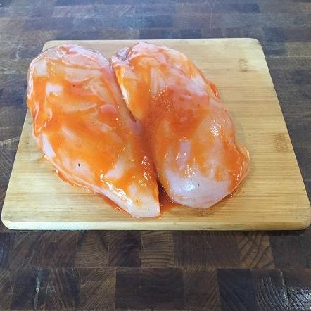 Two chicken breasts in a red marinade on a wooden board