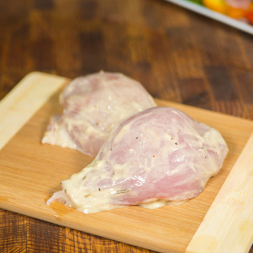 Two marinated chicken breasts on a wooden board
