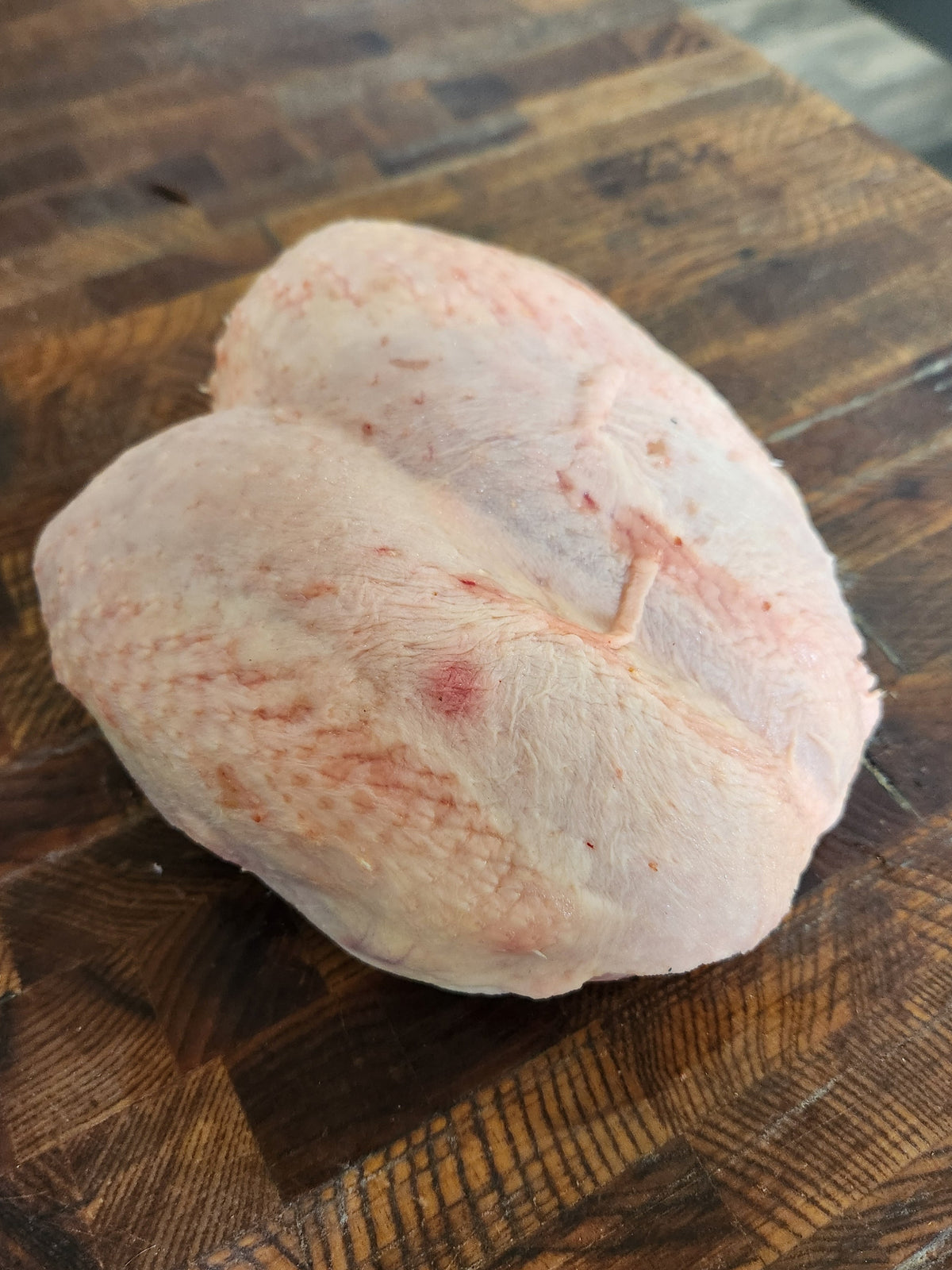 Single raw bone-in chicken breast crown on a wooden butcher block